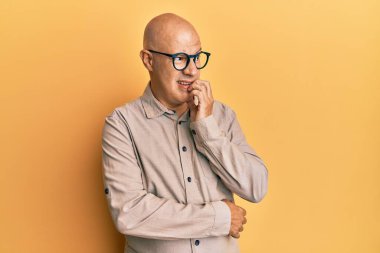 Orta yaşlı kel bir adam, günlük kıyafetler ve gözlük takıyor. Stresli ve gergin görünüyor. Elleri ağızdan tırnak yiyor. anksiyete. 