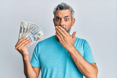 Orta yaşlı, kır saçlı, dolarlar tutan, ağzı ağızla kaplı, şok olmuş ve hata yapmaktan korkan bir adam. şaşırmış ifade 