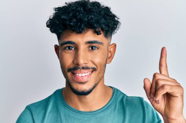 Gündelik kıyafetler giymiş genç Arap yakışıklı bir adam bir fikre ya da soru işaretine şaşırdı ve mutlu bir yüzle işaret etti. 