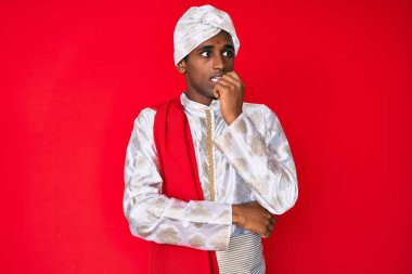 Geleneksel Sherwani sari giysisi giyen yakışıklı Hintli adam gergin ve elleri ağızda tırnak yerken gergin görünüyor. anksiyete. 