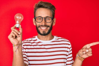 İlham ve fikir için elinde ampul tutan yakışıklı beyaz adam mutlu bir şekilde elini ve parmağını yana doğru uzattı. 