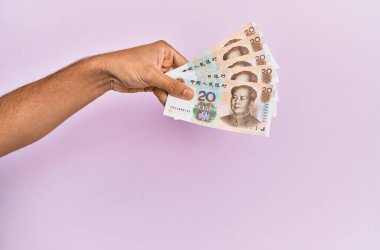 Hispanik el 20 Yuan 'lık Çin banknotunu soyutlanmış pembe arka planda tutuyor.