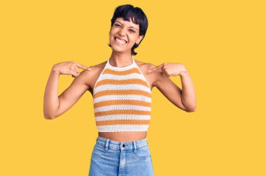 Kısa saçlı, kısa saçlı, kendine güvenen, gülümseyen, kendini gururlu ve mutlu gösteren genç esmer kadın.. 