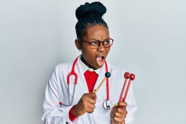 Genç Afro-Amerikalı kadın doktor üniforması giyiyor çatalı ayarlıyor kızgın ve kızgın çığlık atıyor sinirli ve öfkeli, öfkeyle bağırıyor. öfke ve agresif konsept. 