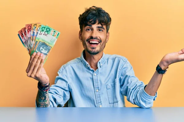 Joven Hispano Sosteniendo Dólares Australianos Sentado Mesa Celebrando Logro Con —  Fotos de Stock