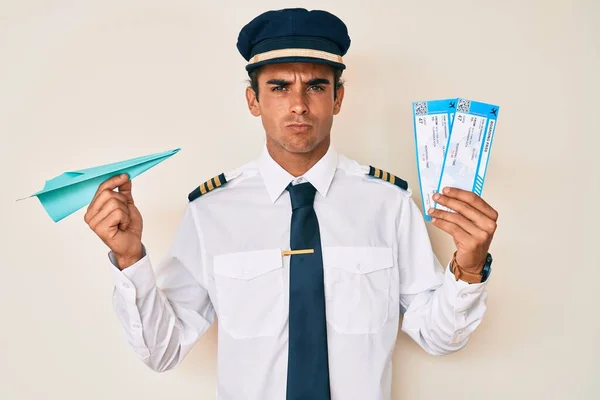 Junger Hispanischer Mann Flugzeugpilotenuniform Mit Papierflugzeug Und Bordkarte Skeptisch Und — Stockfoto