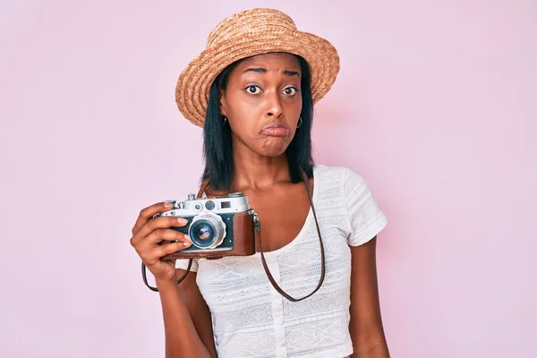 Young african american woman wearing summer hat holding vintage camera depressed and worry for distress, crying angry and afraid. sad expression.