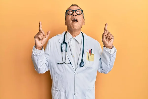 印度中年男子穿着医生的外套和听诊器 惊讶地抬起头 用手指和胳膊指指 — 图库照片