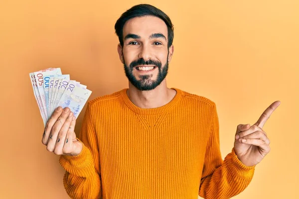 Joven Hispano Sosteniendo Billetes Corona Sueca Sonriendo Feliz Señalando Con — Foto de Stock