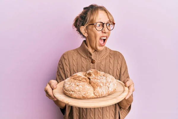 Middle Age Blonde Woman Holding Bread Angry Mad Screaming Frustrated — Stockfoto