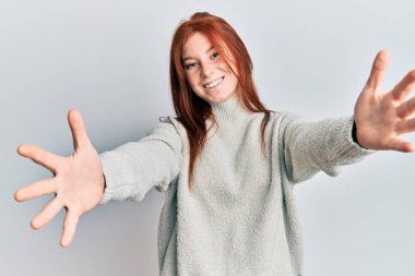 Genç kızıl saçlı kız, sıradan bir kazak giyip kameraya bakıyor ve sarılmak için kollarını açmış gülümsüyor. Mutluluğu kucaklayan neşeli bir ifade.. 