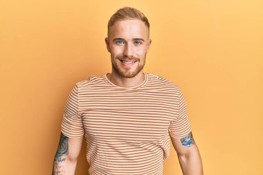 Yüzünde mutlu ve havalı bir gülümseme olan sıradan çizgili tişört giyen genç beyaz bir adam. şanslı kişi. 