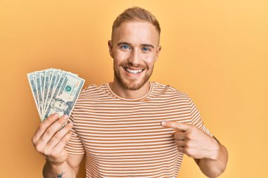 Dolarları tutan genç beyaz adam mutlu bir şekilde elini ve parmağını gösterdi. 