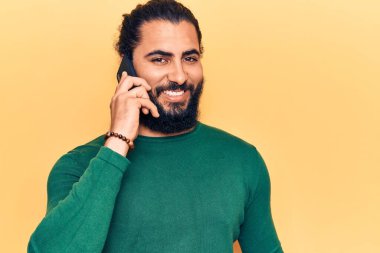 Genç Arap adam akıllı telefondan konuşuyor. Olumlu ve mutlu görünüyor. Kendine güvenen bir gülümsemeyle dişlerini gösteriyor. 