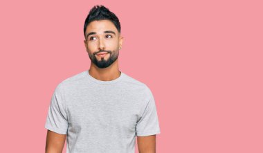 Sakallı, sıradan gri tişörtlü genç adam gülümseyip yan tarafa bakıyor ve düşünüyor.. 