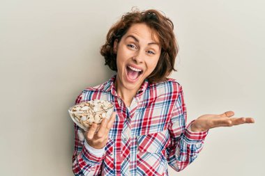 Genç esmer kadın elinde balkabağı tohumlarıyla başarıyı mutlu bir gülümsemeyle kutluyor ve kazanan el kaldırarak ifade ediyor. 