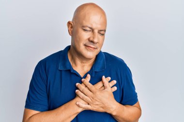 Orta yaşlı, kel, sıradan kıyafetler giyen, elleri göğsünde gülümseyen, gözleri kapalı, yüzünde minnet ifadesi olan bir adam. sağlık kavramı. 