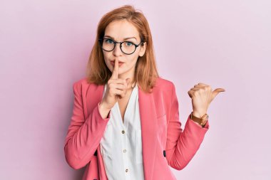 İş stili ve gözlük takan beyaz bir kadın sessiz olmak istiyor. Parmakları dudaklarında, elleri yanda. sessizlik ve gizli konsept. 