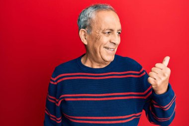 Üst düzey İspanyol adam, günlük kıyafetler giyip baş parmağını yana kaldırıyor ve ağzı açık gülümsüyor. 