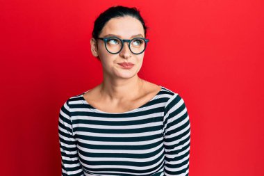 Gündelik kıyafetler ve gözlük takan genç beyaz kadın gülümseyip yan tarafa bakıyor ve düşünüyor.. 