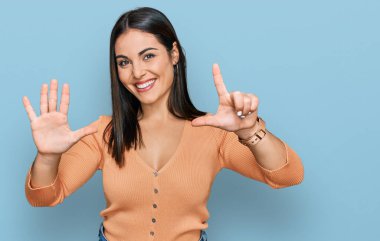 Genç İspanyol kadın gündelik kıyafetler giyer ve yedinci parmaklarını göstererek gülümseyerek mutlu ve kendinden emin bir şekilde gösterir.. 