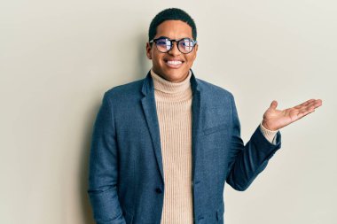 Zarif kıyafetler ve gözlük takan genç, yakışıklı İspanyol adam gülümseyen, elinde avucuyla kameraya bakan ve işaret eden.. 