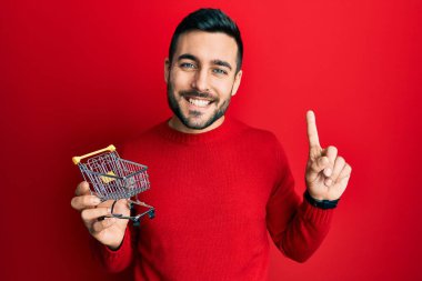 Elinde küçük bir süpermarket arabası olan genç İspanyol bir adam bir fikir ya da soruyla şaşırdı ve mutlu bir yüzle işaret etti. 