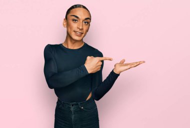 Makyaj yapan ve uzun saçlı İspanyol transseksüel adam kameraya hayret ediyor ve gülümsüyor.. 