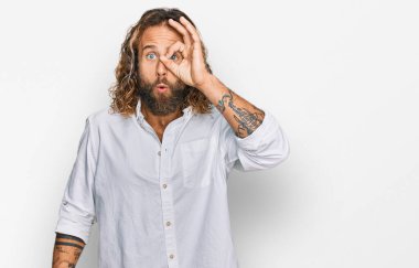 Sakallı, uzun saçlı, sıradan kıyafetler giyen, şaşırmış yüzüyle şaşırmış, parmaklarından bakan yakışıklı bir adam. İnançsız ifade. 