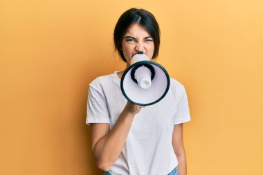 Sarı arka planda megafonu olan genç ve güzel bir kadın kötü bir durumda bağırıyor.