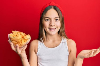 Güzel esmer küçük kız patates cipsi tutuyor başarıyı mutlu bir gülümsemeyle ve kazanan yüz ifadesiyle kutluyor. 