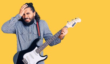 Elektro gitar çalan genç bir Arap. Kafası karışık, şaşırmış ve sinirli bir yüzü var. 