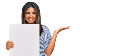 Boş afiş tutan genç Latin kız zaferi mutlu bir gülümsemeyle ve kazanan yüz ifadesiyle kutluyor. 