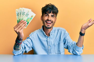 Masada oturan İspanyol asıllı genç adam başarıyı mutlu bir gülümsemeyle ve elini kaldırarak kutluyor. 