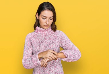 Yün kazak giyen genç beyaz kız kol saatini kontrol ediyor, gevşemiş ve kendinden emin. 