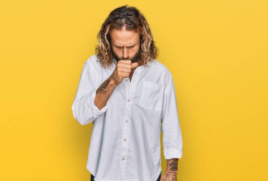 Sakallı, uzun saçlı, günlük kıyafetler giyen, kendini iyi hissetmeyen ve soğuk algınlığı veya bronşitin belirtisi olarak öksüren yakışıklı bir adam. sağlık hizmeti kavramı. 