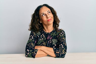 Orta yaşlı, güzel bir kadın. Günlük kıyafetler giymiş. Masaya oturmuş gülümsüyor.. 