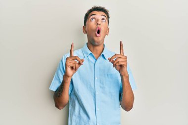 Genç, yakışıklı, Afro-Amerikalı, günlük kıyafetler giymiş. Şaşırmış ve şaşırmış. Parmaklarıyla işaret ediyor ve kollarını kaldırıyor.. 