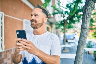 Orta yaşlı yakışıklı adam şehirde akıllı telefon kullanarak mutlu gülümsüyor..