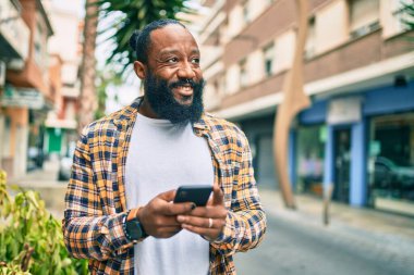 Sakallı Afrikalı Amerikalı adam akıllı telefon kullanıyor. Yazıyor, mesaj yazıyor, gülümsüyor.