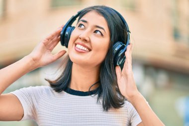Genç İspanyol kadın gülümseyerek şehirde kulaklık takarak müzik dinliyor..