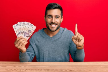 Meksika pesolarını elinde tutan yakışıklı İspanyol bir adam bir fikir veya soruyla gülümsüyor ve mutlu bir yüzle işaret ediyor. 