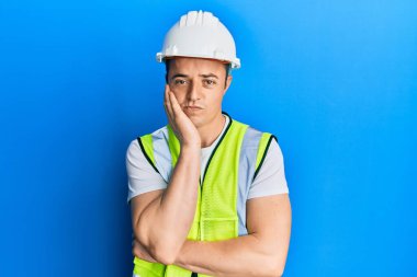 Güvenlik kaskı takan yakışıklı genç adam kollarını kavuşturarak depresyondan sıkılmış ve yorgun gözüktüğünü düşünüyor.. 