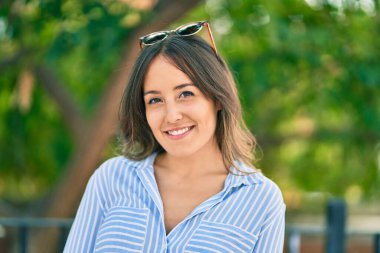 Genç İspanyol kadın gülümsüyor. Parkta güneş gözlüğüne dokunduğu için mutlu..