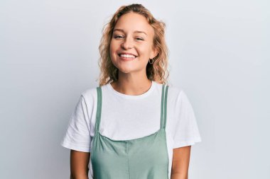 Güzel, beyaz bir kadın günlük kıyafetler giyiyor. Pozitif ve mutlu görünüyor. Kendine güvenen bir gülümsemeyle dişlerini gösteriyor. 