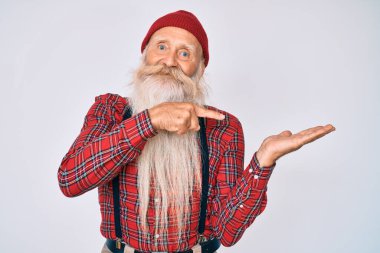 Gri saçlı ve uzun sakallı yaşlı bir adam. Hipster görünümlü, yün şapkalı. Kameraya hayret ediyor ve gülümsüyor.. 