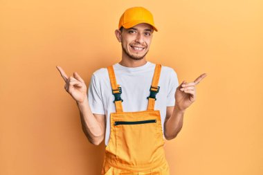 Tamirci üniforması giyen, kendine güvenen, parmakları farklı yönleri gösteren İspanyol bir genç. reklam için kopyalama alanı 