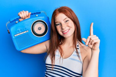 Genç kızıl saçlı kız elinde klasik bir radyoyla gülümsüyor bir fikir ya da soru işareti ile mutlu bir yüzle, bir numara 