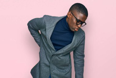 Genç Afro-Amerikan adam iş kıyafetleri ve gözlük takıyor sırt ağrısı çekiyor, elleriyle dokunuyor, kas ağrısı çekiyor. 