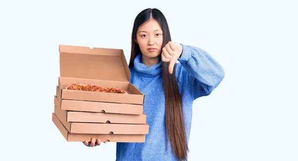 年轻美丽的中国女人手里拿着一盒装意大利披萨的纸盒 满脸怒容 消极的迹象表明她不喜欢大拇指朝下 拒绝的概念 — 图库照片